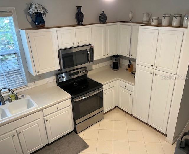 kitchen featuring sink, white cabinets, light tile patterned floors, and appliances with stainless steel finishes