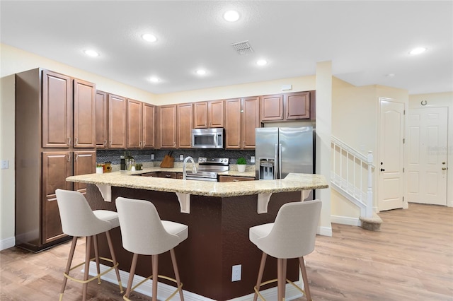 kitchen with tasteful backsplash, a kitchen island with sink, a kitchen bar, light hardwood / wood-style floors, and stainless steel appliances