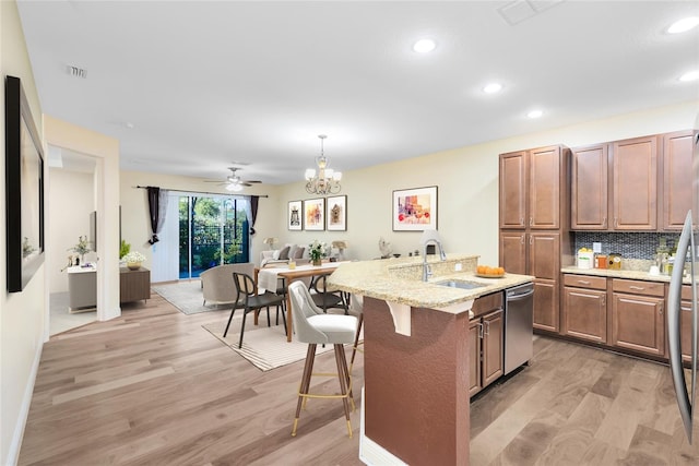 kitchen with decorative light fixtures, sink, a kitchen breakfast bar, light wood-type flooring, and a center island with sink