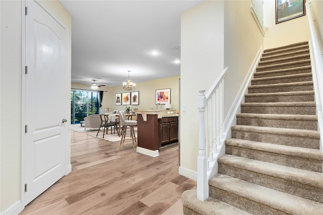 stairway with hardwood / wood-style flooring and ceiling fan with notable chandelier