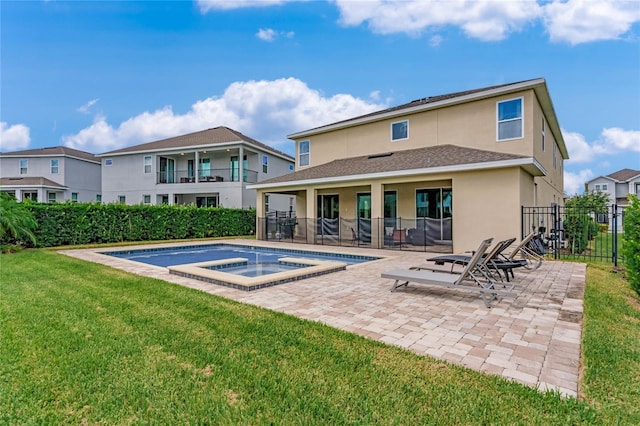 back of property with a swimming pool with hot tub, a patio, and a lawn