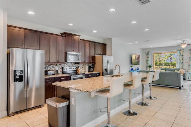 kitchen with appliances with stainless steel finishes, sink, a kitchen island with sink, and a breakfast bar area