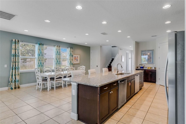 kitchen featuring appliances with stainless steel finishes, sink, a kitchen island with sink, light tile patterned floors, and dark brown cabinetry