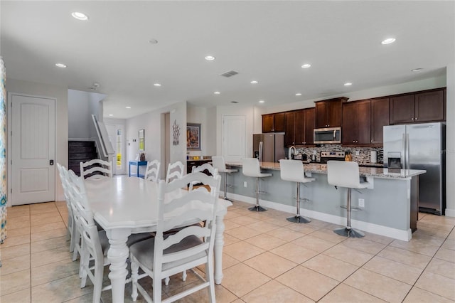 kitchen with dark brown cabinetry, a kitchen bar, light tile patterned floors, stainless steel appliances, and a kitchen island with sink