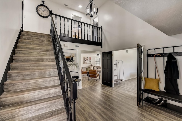 stairway featuring hardwood / wood-style floors, ceiling fan with notable chandelier, and high vaulted ceiling