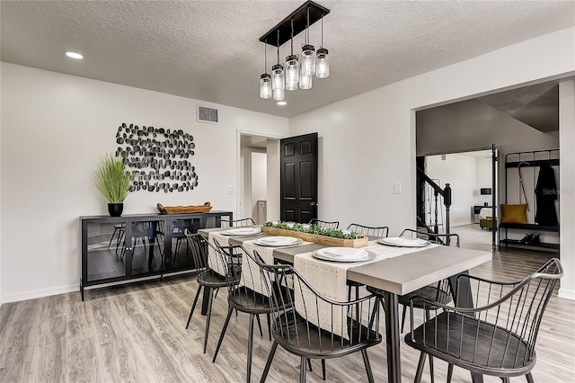 dining room with a textured ceiling, a notable chandelier, and light wood-type flooring