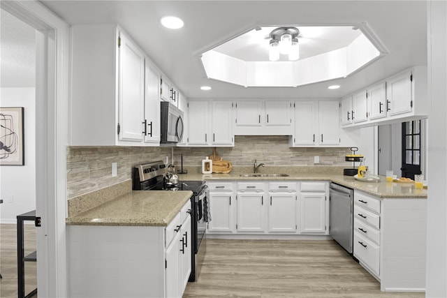 kitchen featuring appliances with stainless steel finishes, white cabinets, light wood-type flooring, sink, and light stone counters