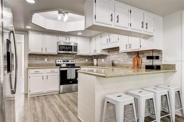 kitchen with a breakfast bar, white cabinetry, appliances with stainless steel finishes, and kitchen peninsula