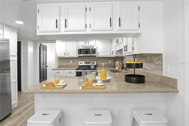 kitchen featuring white cabinetry, stainless steel appliances, decorative backsplash, kitchen peninsula, and light stone counters