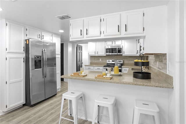 kitchen with kitchen peninsula, light hardwood / wood-style flooring, appliances with stainless steel finishes, white cabinets, and a kitchen bar