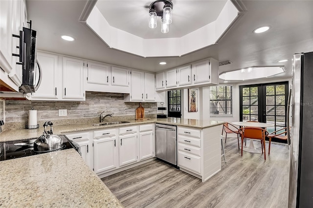 kitchen featuring white cabinets, appliances with stainless steel finishes, sink, kitchen peninsula, and a tray ceiling