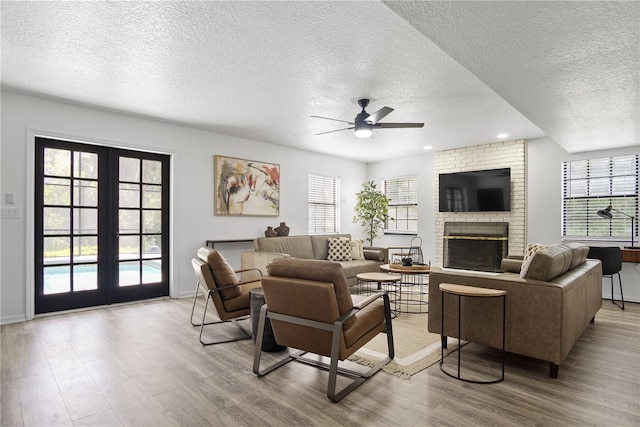 living room featuring a textured ceiling, french doors, a fireplace, ceiling fan, and light hardwood / wood-style flooring