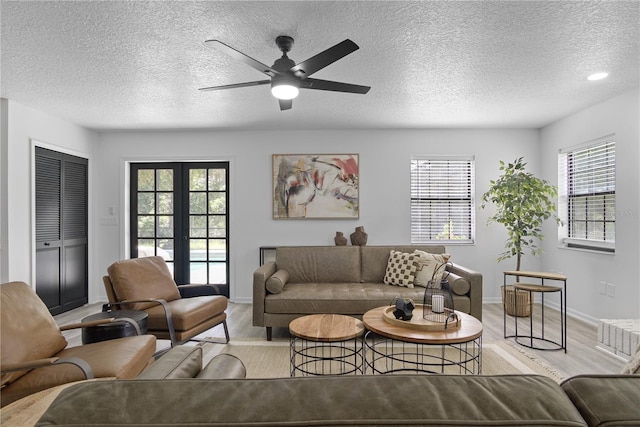 living room featuring ceiling fan, french doors, light hardwood / wood-style floors, and a textured ceiling