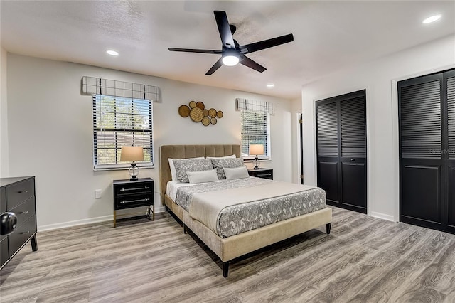 bedroom featuring ceiling fan, light hardwood / wood-style floors, and multiple closets