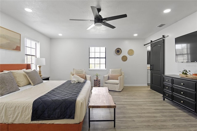 bedroom with ceiling fan, a barn door, and wood-type flooring