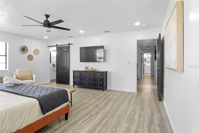 bedroom featuring light wood-type flooring, ceiling fan, a barn door, and ensuite bath