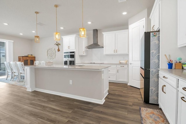 kitchen featuring decorative light fixtures, white cabinets, refrigerator, and wall chimney exhaust hood