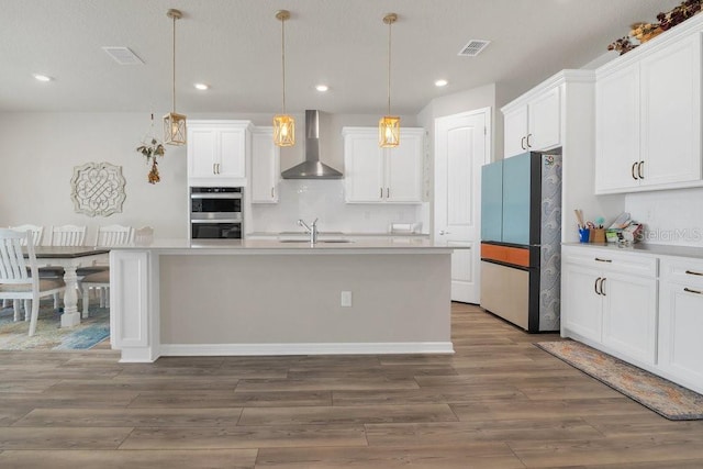 kitchen with fridge, white cabinetry, and wall chimney range hood