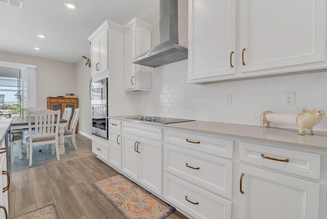 kitchen with white cabinetry, black electric stovetop, light hardwood / wood-style floors, decorative backsplash, and wall chimney range hood