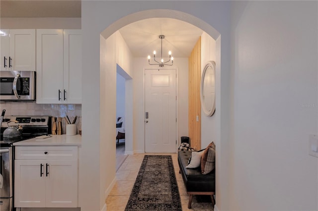 doorway featuring arched walkways, a notable chandelier, baseboards, and light tile patterned floors