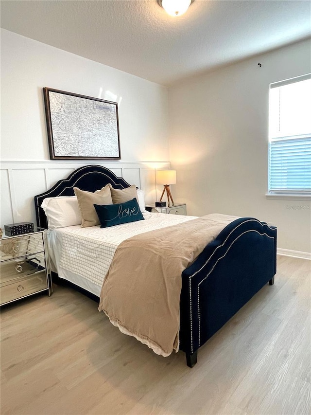 bedroom with a textured ceiling, wood finished floors, and a decorative wall