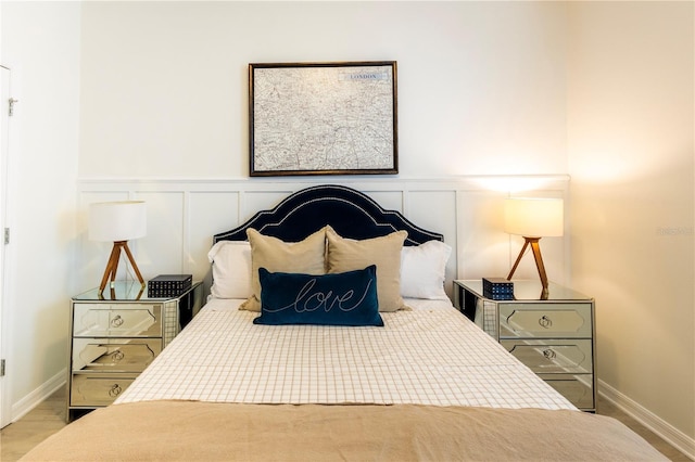 bedroom with wainscoting, a decorative wall, and wood finished floors