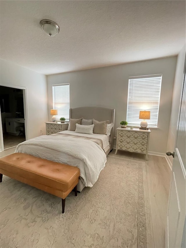 bedroom featuring baseboards, light wood-style flooring, and a textured ceiling