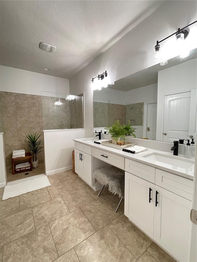 bathroom with a textured ceiling, double vanity, walk in shower, and a sink