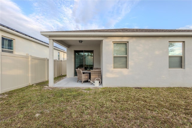 rear view of house featuring a yard, a patio area, fence, and stucco siding