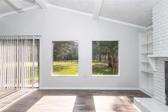 empty room featuring a brick fireplace, plenty of natural light, dark hardwood / wood-style flooring, and vaulted ceiling with beams