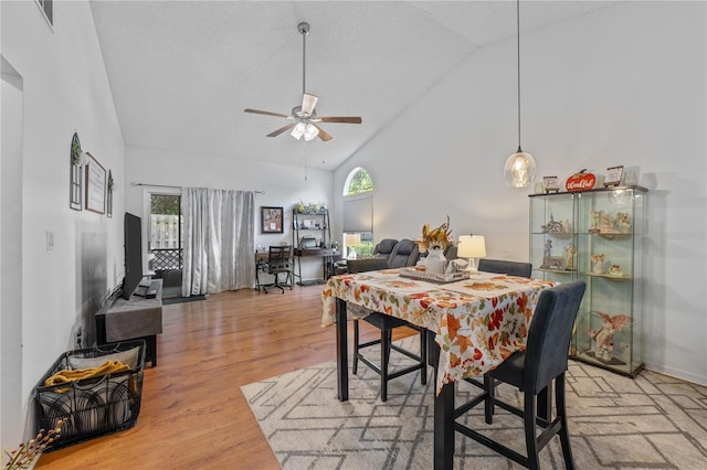 dining space with ceiling fan, hardwood / wood-style floors, and high vaulted ceiling