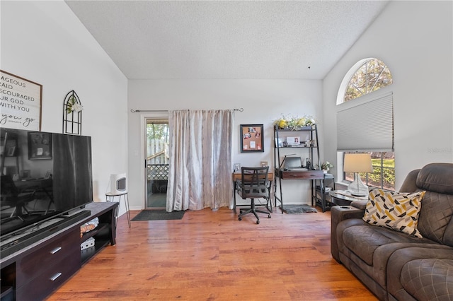 living room featuring light hardwood / wood-style floors, a textured ceiling, and a towering ceiling