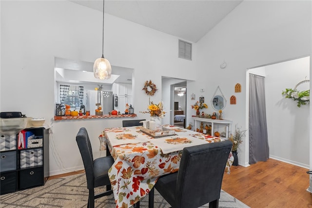 dining room with high vaulted ceiling and light hardwood / wood-style flooring