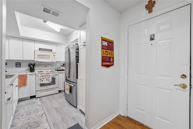 kitchen with white cabinetry, backsplash, white appliances, and light wood-type flooring