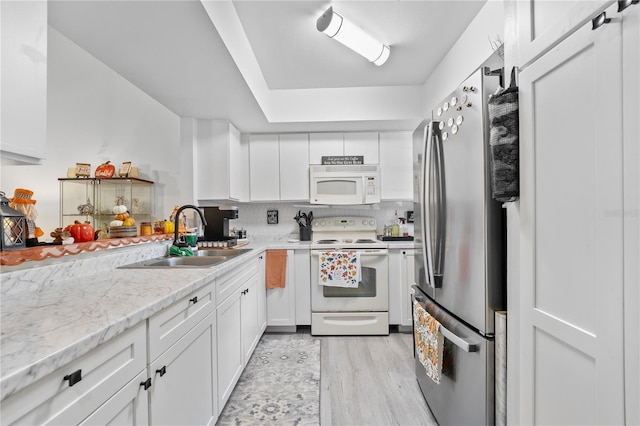 kitchen featuring white appliances, white cabinetry, sink, backsplash, and light stone counters