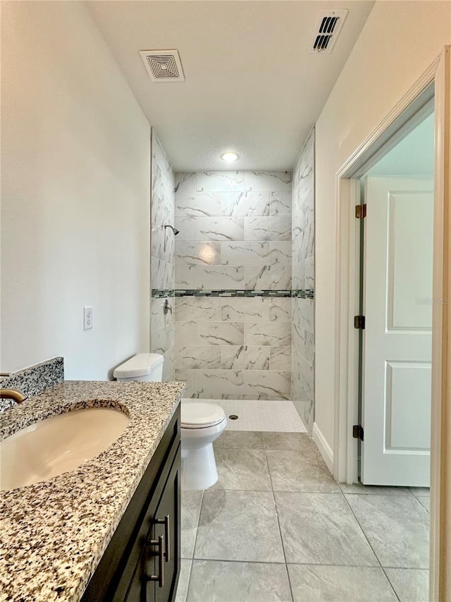 bathroom with a tile shower, vanity, and toilet