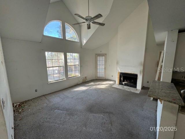 unfurnished living room featuring high vaulted ceiling, plenty of natural light, ceiling fan, and carpet flooring