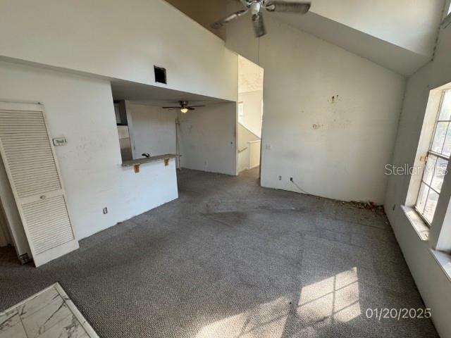 unfurnished living room with high vaulted ceiling, dark carpet, and ceiling fan