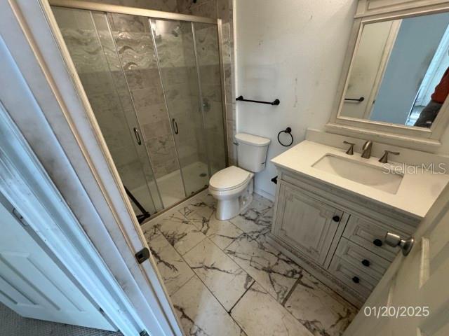 bathroom featuring a shower with door, toilet, and vanity