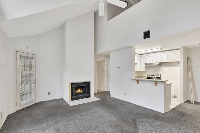 unfurnished living room with dark colored carpet, high vaulted ceiling, a fireplace with flush hearth, and a ceiling fan