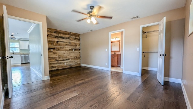 unfurnished bedroom featuring ensuite bath, wooden walls, a closet, dark hardwood / wood-style flooring, and ceiling fan