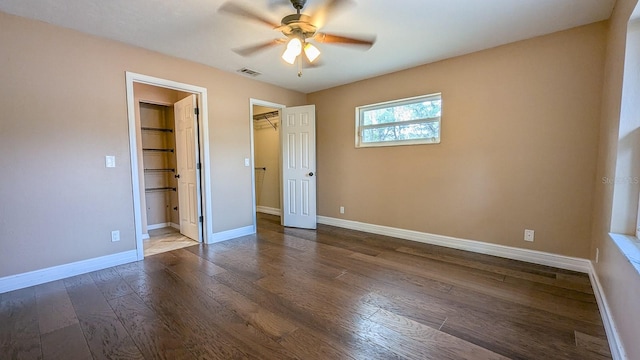 unfurnished bedroom featuring ceiling fan, dark wood-type flooring, a closet, and a walk in closet