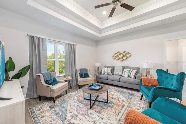 living room featuring ceiling fan, hardwood / wood-style floors, a tray ceiling, and ornamental molding