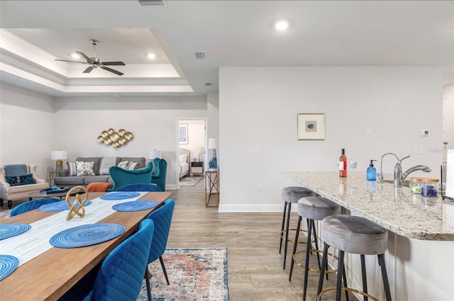 dining area featuring ceiling fan, light hardwood / wood-style flooring, crown molding, and a tray ceiling