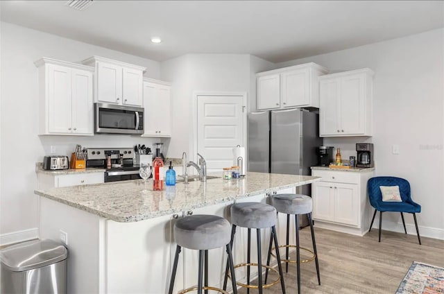 kitchen with stainless steel appliances, white cabinetry, and a kitchen island with sink