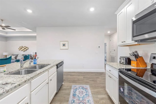 kitchen featuring appliances with stainless steel finishes, sink, white cabinets, light stone countertops, and light hardwood / wood-style floors