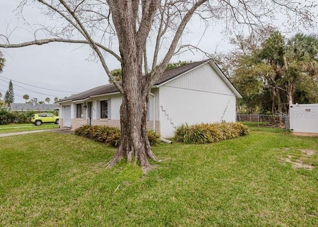 view of side of property featuring fence, a lawn, and brick siding