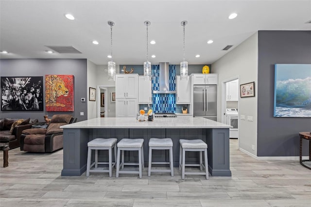 kitchen featuring white cabinetry, a large island, built in refrigerator, pendant lighting, and wall chimney exhaust hood