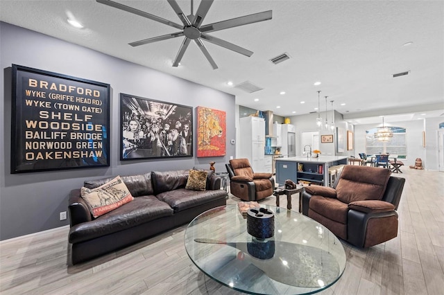 living room featuring ceiling fan, a textured ceiling, and light hardwood / wood-style flooring