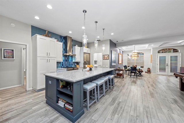 kitchen with a large island, white cabinets, french doors, pendant lighting, and wall chimney exhaust hood